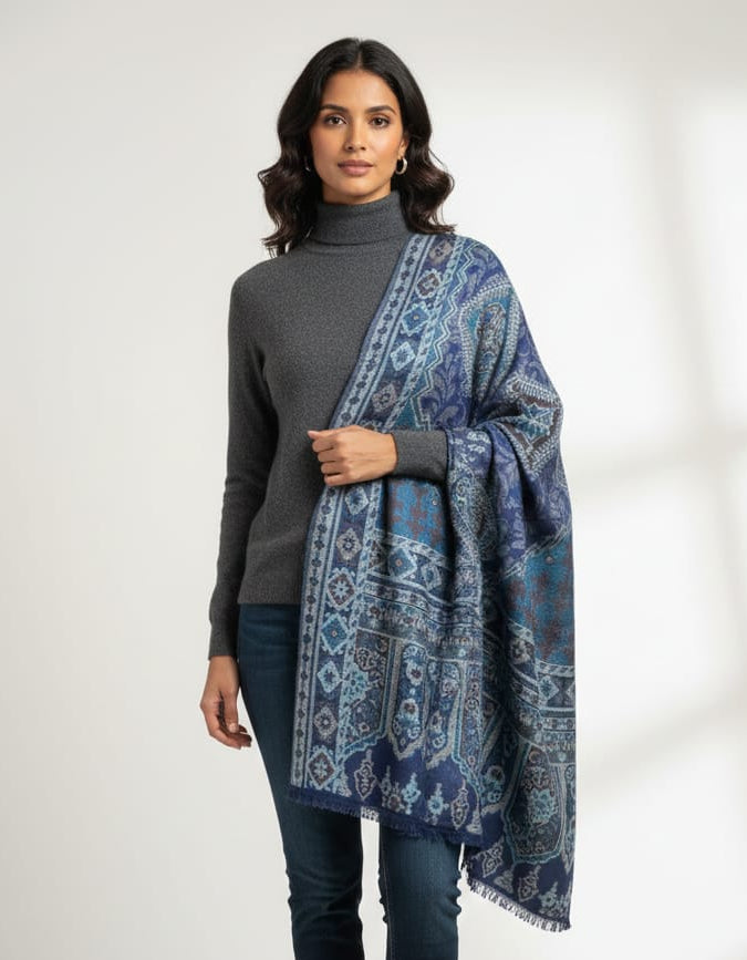 Woman in a grey turtleneck and denim wearing a deep indigo and glacial blue Kaani pashmina shawl with intricate geometric weaving.